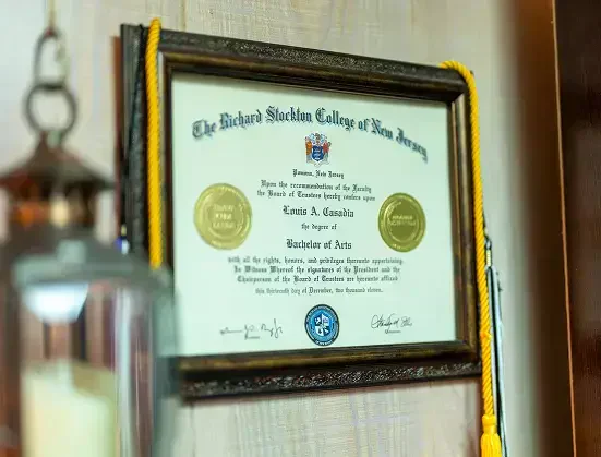 Diploma enmarcado del Richard Stockton College de Nueva Jersey, otorgado a Louis A. Casadia para Licenciatura en Artes, con sellos de oro.