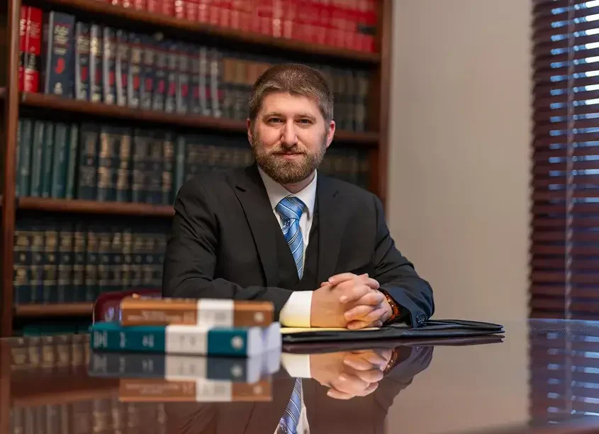 Louis Casadia in a suit sits at a polished desk, surrounded by law books, conveying a professional legal setting